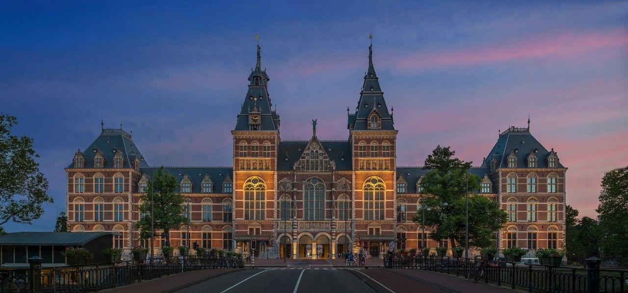 Rijksmuseum in Amsterdam bij avondlicht, gezien vanaf de brug met de verlichte gevel en torens.