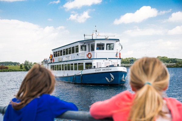 Meisjes kijken naar de rondvaartboot die aanmeert in de gemeente Maasgouw
