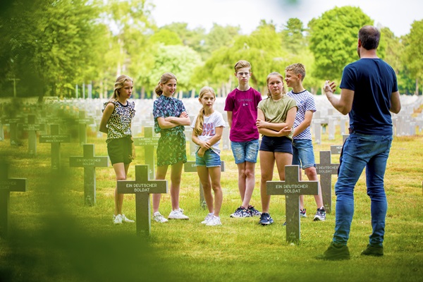 Kinderen luisteren naar de verhalen van de gids op het Duitse Oorlogsbegraafplaats