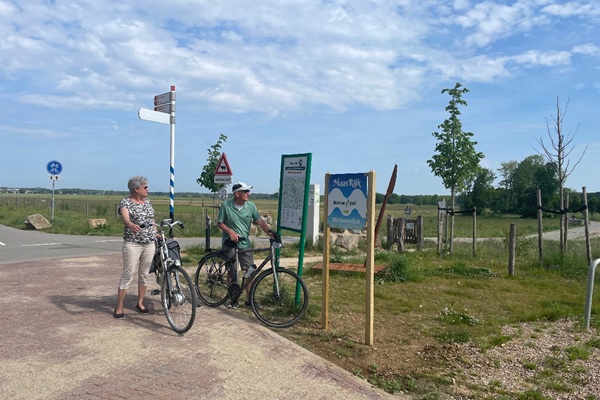 Fietsers bekijken een routebord op een kruispunt in het buitengebied van Venray, onder een blauwe lucht.