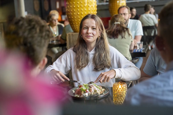 Meisje kijkt recht in de camera terwijl ze bezig is om haar carpacchio te snijden