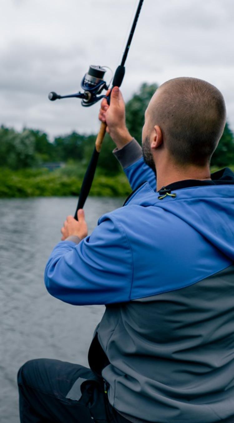 Man aan het vissen vanaf de oever met een hengel boven het water op een bewolkte dag in Limburg.