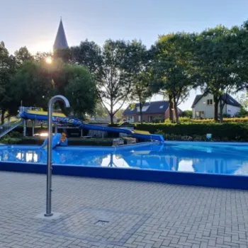 Op de voorgrond het buitenbad van zwembad Weerderhof en op de achtergrond woonhuizen en de kerk van Linne.