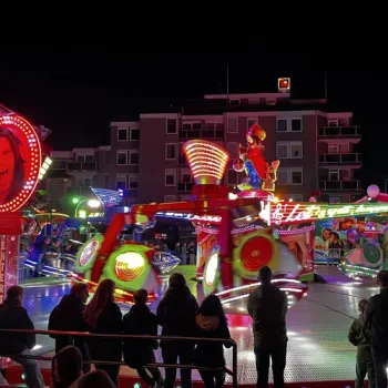 Kleurrijke kermisattractie in Weert bij avond, met bezoekers langs de kant.