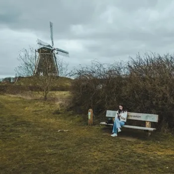 Een vrouw zit op een bankje langs het Huurvaarderspad bij Beesel, met een traditionele windmolen op de achtergrond.